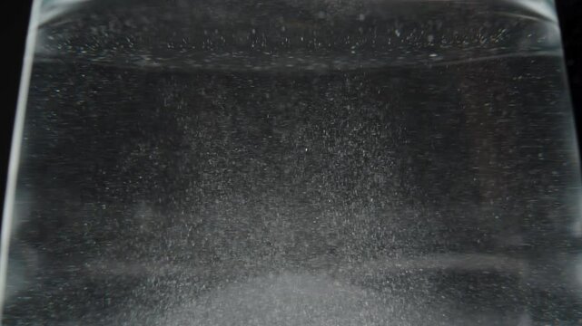 Undissolved particles of the powder swirling in a glass of water, slowly mixing and settling.