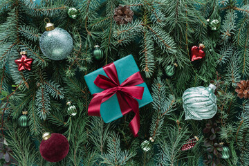 Wrapped gift box tied with a ribbon on a background of Assorted coniferous branches decorated with festive Christmas baubles