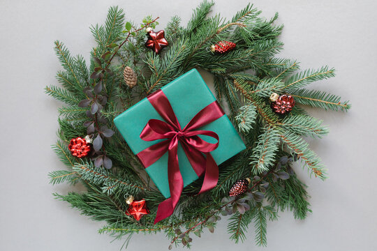 Overhead view of a wrapped gift box in the middle of a coniferous Christmas wreath decorated with christmas baubles