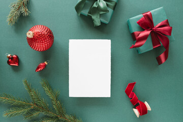 Overhead view of a blank piece of deckle edge card  with a wrapped Christmas gift and assorted Christmas decorations on a green background