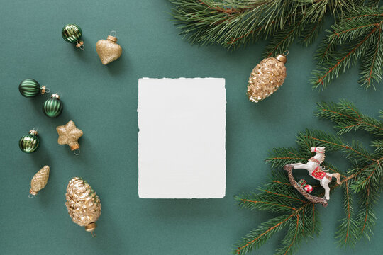 Overhead view of a blank piece of deckle edge card  with assorted Christmas decorations, ornaments and pine branches on a green background