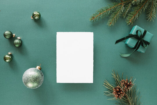 Overhead view of a blank piece of deckle edge card  with a wrapped Christmas gift, pine branches and assorted Christmas decorations on a green background