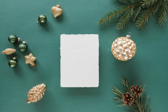 Overhead view of a blank piece of deckle edge card  with assorted Christmas decorations, ornaments and pine branches on a green background