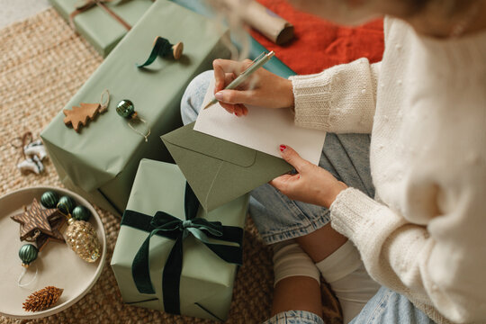 Overhead view of a woman sitting cross-legged on the floor writing invitations and wrapping Christmas gifts