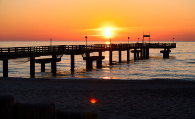 Obraz premium Sun setting behind a pier at the Baltic Sea on a spring night in northern Germany.