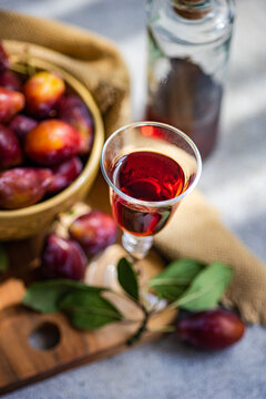 Overhead view of a Bowl of freshly picked ripe red plums and a glass and bottle of homemade plum liqueur on a wooden chopping board