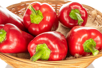 Several sweet red peppers in a straw bowl, macro, isolated on white background.