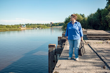 Fototapeta premium An elderly woman stands on an old abandoned river pier.