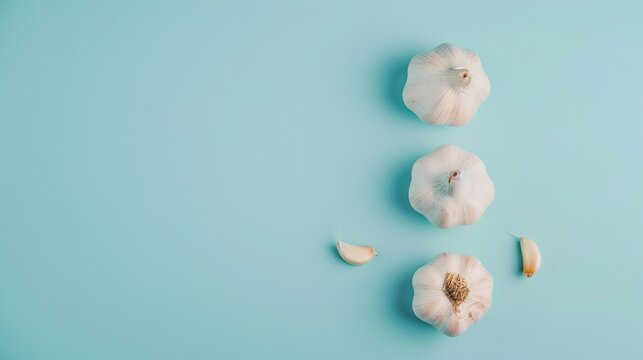 Three whole garlic bulbs with a few cloves, arranged artistically on a pastel blue background, emphasizing simplicity and culinary elegance.