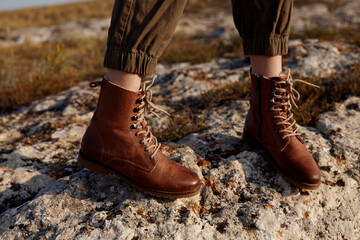 Brown boots standing on rock in the middle of field with grass and trees in background, nature travel fashion concept