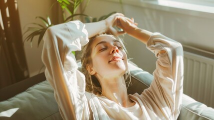 Fototapeta premium A woman relaxes on a couch with her eyes closed, basking in the warm sunlight streaming through a nearby window, embodying tranquility and contentment.