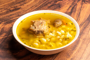 Close up to a bowl of soup Traditional Bolivian food, pork soup called fricase, white bowl on a rustic wooden table