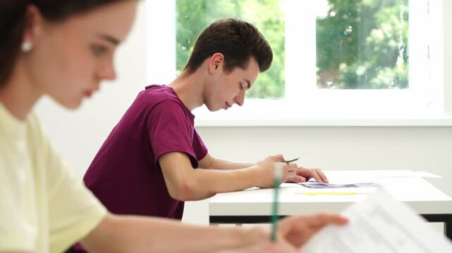 High school teenagers in classroom girl and boy sitting at desks writing exam doing test, checking answers, close up. Modern education concept.