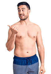 Fototapeta premium Young handsome man wearing swimwear smiling with happy face looking and pointing to the side with thumb up.