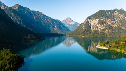 Fototapeta premium Tranquil reflections in Lake Plansee surrounded by majestic mountains in Austria's alpine landscape