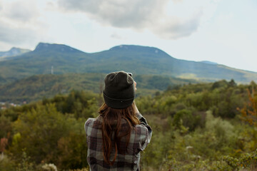 A stylish woman in a plaid shirt and hat enjoying the breathtaking beauty of mountain scenery