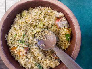 Bulgur cooked with green pepper, onion and parsley in a ceramic bowl on the table during dinner. Homemade dishes. The concept of traditional Turkish cuisine. Horizontal orientation. Top view.