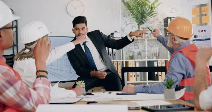 Man manager of building company explaining project on glass wall for engineers constructors during meeting.