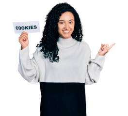 Young hispanic woman with curly hair holding cookies banner smiling happy pointing with hand and finger to the side