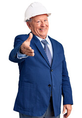 Senior handsome grey-haired man wearing suit and architect hardhat smiling friendly offering handshake as greeting and welcoming. successful business.