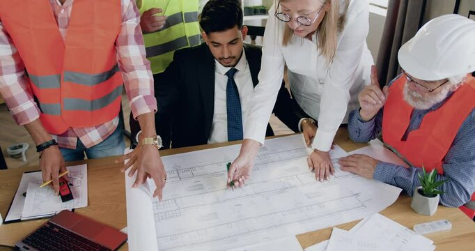 Diverse team of architects at the head with successful man main architect working together over blueprint of new building