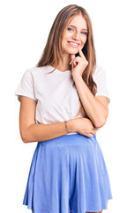 Young beautiful blonde woman wearing summer style looking confident at the camera with smile with crossed arms and hand raised on chin. thinking positive.