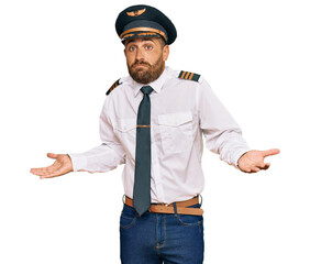 Handsome man with beard wearing airplane pilot uniform clueless and confused expression with arms and hands raised. doubt concept. © Krakenimages.com