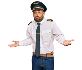 Handsome man with beard wearing airplane pilot uniform clueless and confused expression with arms and hands raised. doubt concept.