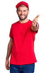 Young handsome blond man wearing t-shirt and cap smiling friendly offering handshake as greeting and welcoming. successful business.