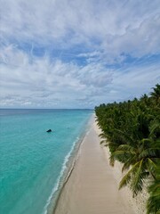The photo shows an aerial view of Dhigurah Island in the Maldives, featuring a long stretch of lush greenery bordered by pristine white sand beaches and crystal-clear turquoise waters. 