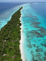 The photo shows an aerial view of Dhigurah Island in the Maldives, featuring a long stretch of lush greenery bordered by pristine white sand beaches and crystal-clear turquoise waters. 