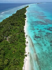 The photo shows an aerial view of Dhigurah Island in the Maldives, featuring a long stretch of lush greenery bordered by pristine white sand beaches and crystal-clear turquoise waters. 