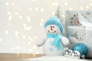 Funny snowman figure and other Christmas decor on artificial snow against blurred lights, space for...