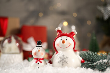 Funny snowmen figures and fir branch on artificial snow, closeup