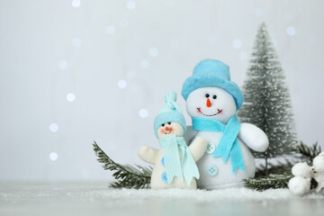 Cute decorative snowmen and fir branches on artificial snow against blurred lights. Space for text