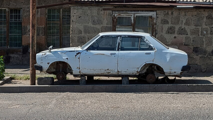 Naklejka premium An old, rusty car stands on bricks on the side of the road.