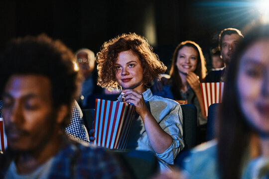 Young woman watching movie in theater with popcorn audience in background