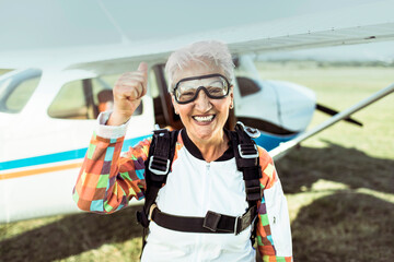 Smiling senior woman giving thumbs up before skydiving