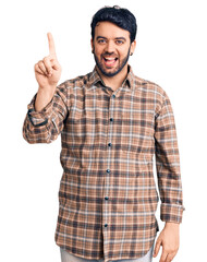Naklejka premium Young hispanic man wearing casual clothes pointing finger up with successful idea. exited and happy. number one.