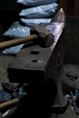  Close-up view of a vintage anvil and hammer in a rustic blacksmith's workshop, showcasing textures and details under dim lighting.