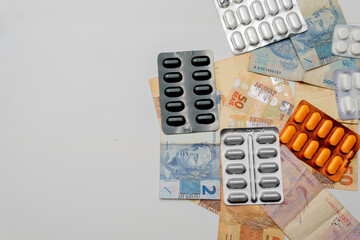 White background with medicines, pills, blister packs and Brazilian real banknotes, concept of...