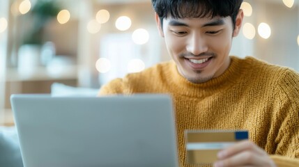 Asian man shopping online in living room, young Korean holding credit card, purchasing clothes, arranging food delivery, focused businessman using laptop.