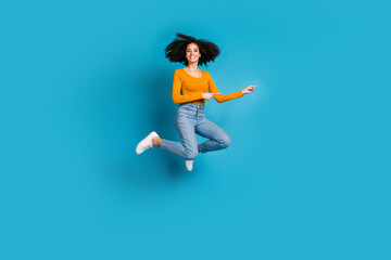 Full body photo of attractive young woman jumping point empty space dressed stylish yellow clothes isolated on blue color background