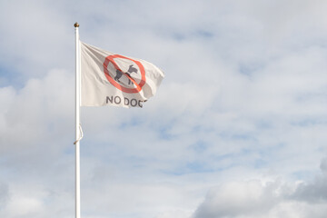 No Dogs flag flying in wind with blue sky and white clouds behind