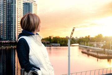Fototapeta premium A woman on the embankment of the river in the city looks at the sunset. Kyiv, Rivermall park