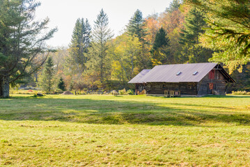 Obraz premium Old wooden barns in a meadow at the foot of a forested hill on a sunny autumn day