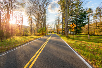 Warning sign on a deserted winding road through a wooded mountain valley at sunset in autumn