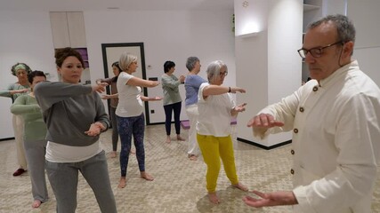 A group of senior women practices mindful movements during a yoga session, led by their instructor. Concept of mindfulness, physical health, and movement for seniors.