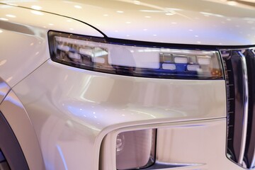 Close up on headlight of modern SUV automobile. White demo vehicle with pearlescent shine displayed in car showroom at dealership center