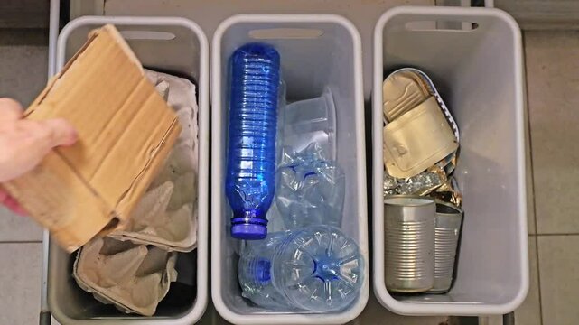 A man segregating paper, plastic and metal household garbage throwing it into three separate trash bins